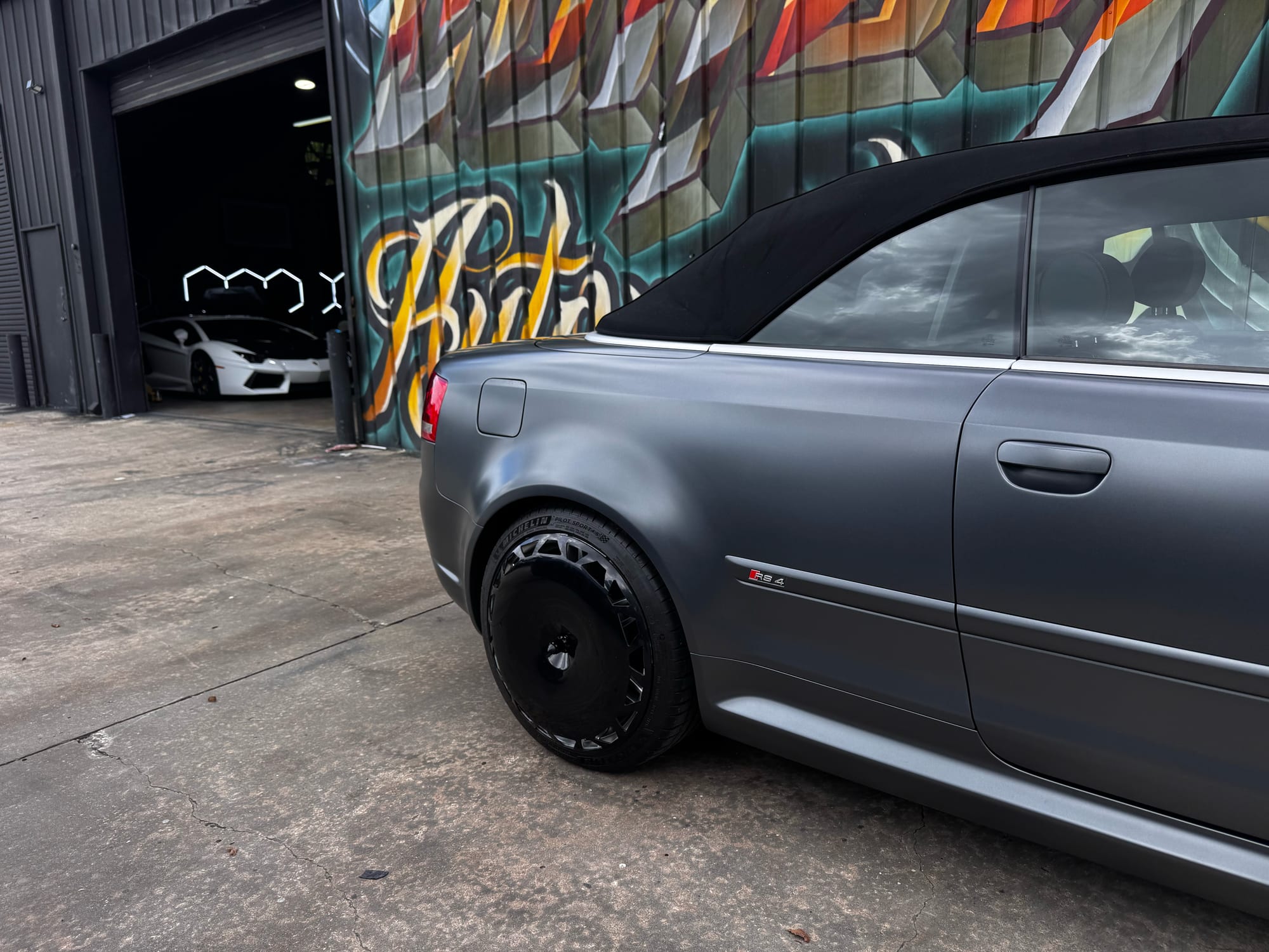 Rear quarter of a matte grey Audi RS4 cabriolet with a gloss black AIRODISC fitted to the rear wheel, outside the Corsa Automotive shop