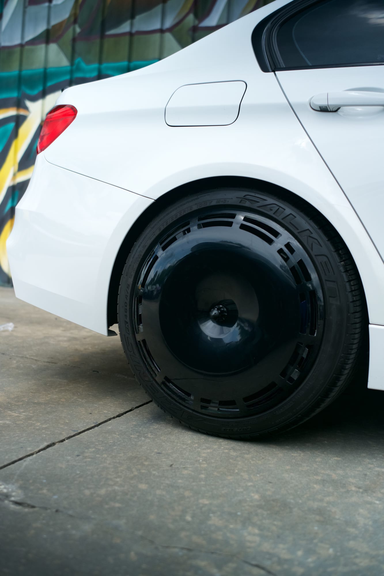 Close view of a gloss black Performance Series AIRODISC, its segmented outer ring visible, fitted to the rear wheel of a white BMW M3