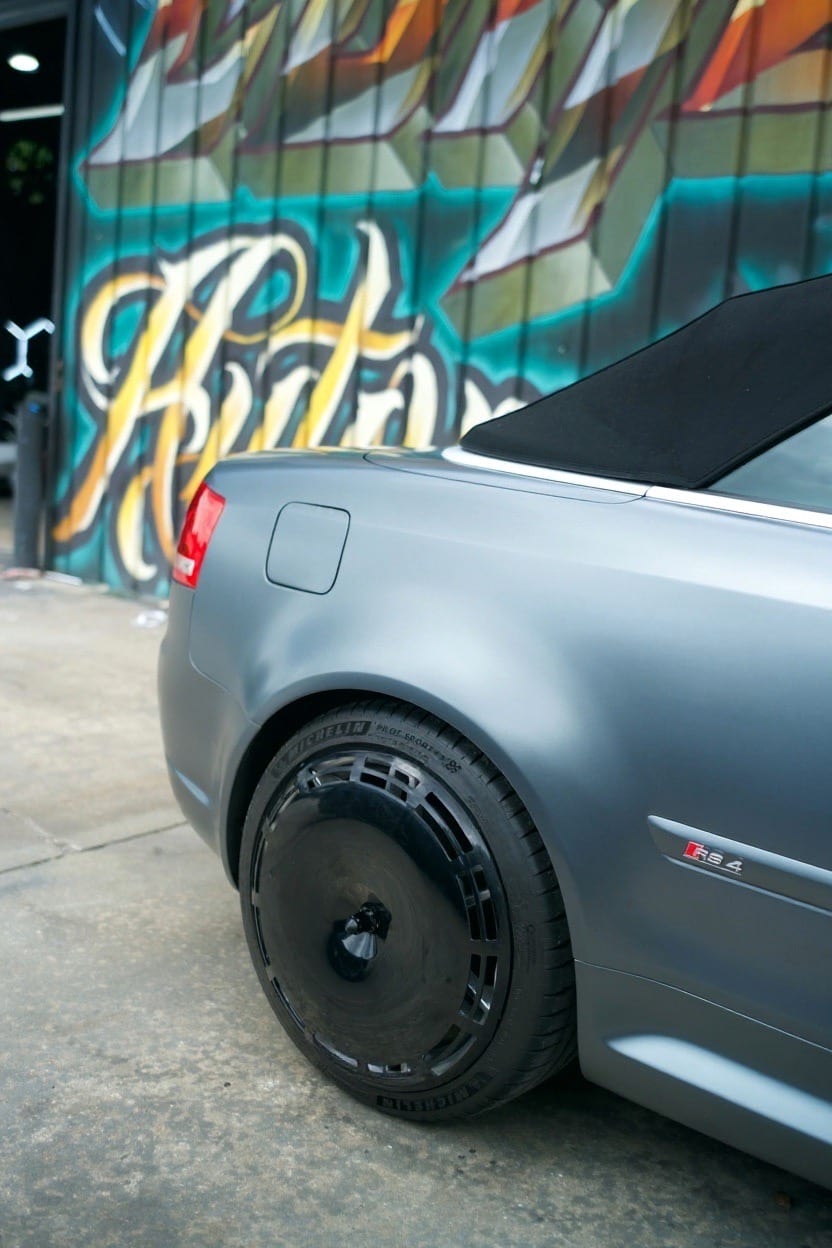 A gloss black AIRODISC mounted on the rear wheel of a silver Audi RS4 cabriolet, with the centre nut visible at the hub