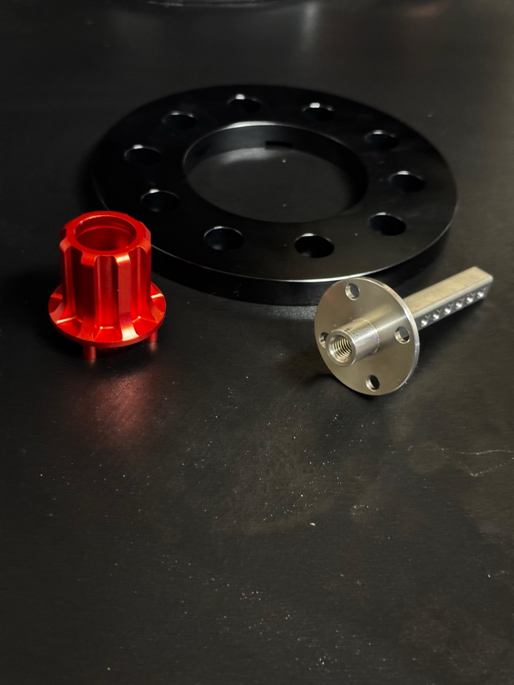 The actual AIRODISC hardware: black bolt-pattern spacer, red anodised centre nut, and machined stainless centre post
